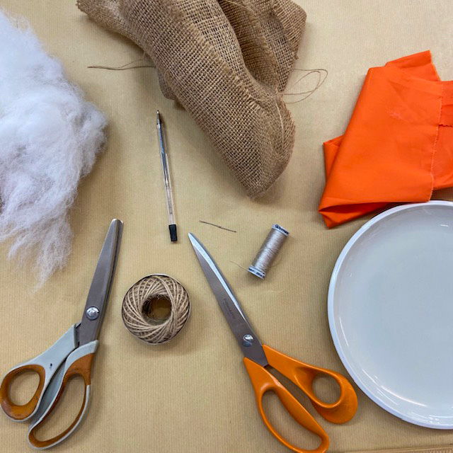 Materials needed. Picture shows scissors, hessian, thread, pen, plate, orange fabric, stuffing material.
