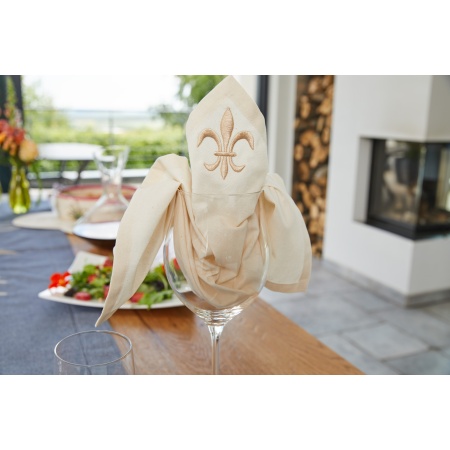 A napkin tucked into a glass on a restaurant table with a design embroidered onto it.