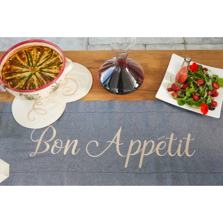 Embroidered table runner with 'Bon Appetit' and food layed out on the table.