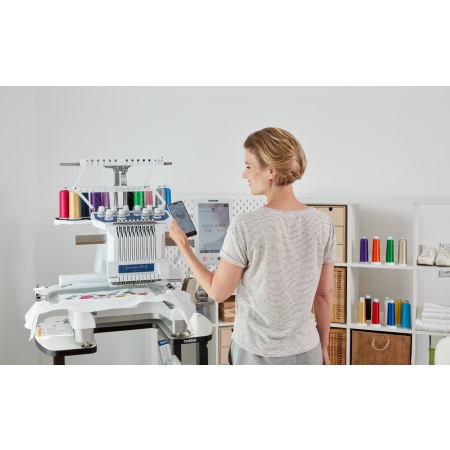Lady stood in front of the Brother PR1055X 10 needle embroidery machine, colourful threads set up ready to stitch.