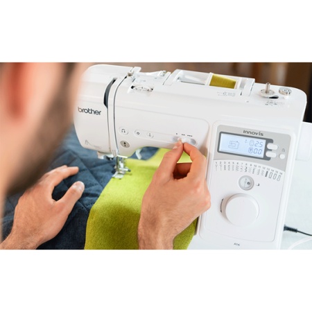 Man sat sewing, fabric under the sewing machine and the speed button beting adjusted on the front panel of the machine